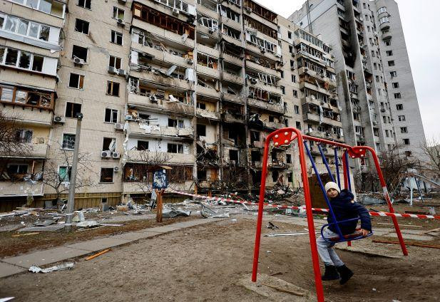 Niño en un columpio frente a un edificio residencial dañado, después de los ataques de Rusia a Ucrania 25-2-22