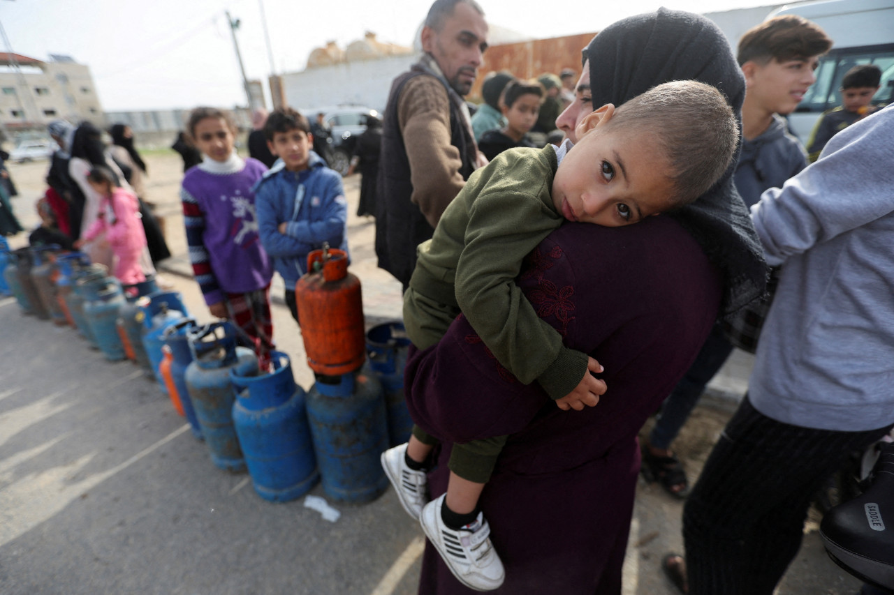 Una mujer lleva a un niño mientras los palestinos se reúnen para llenar bombonas de gas líquido_Gaza_Reuters