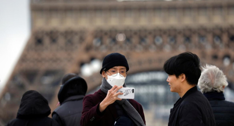 Personas con barbijo frente a la Torre Eiffel por coronavirus, REUTERS