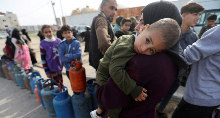 Una mujer lleva a un niño mientras los palestinos se reúnen para llenar bombonas de gas líquido_Gaza_Reuters